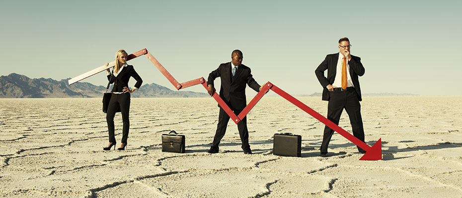 Three business people standing in dry lake bed holding red arrow pointing down.